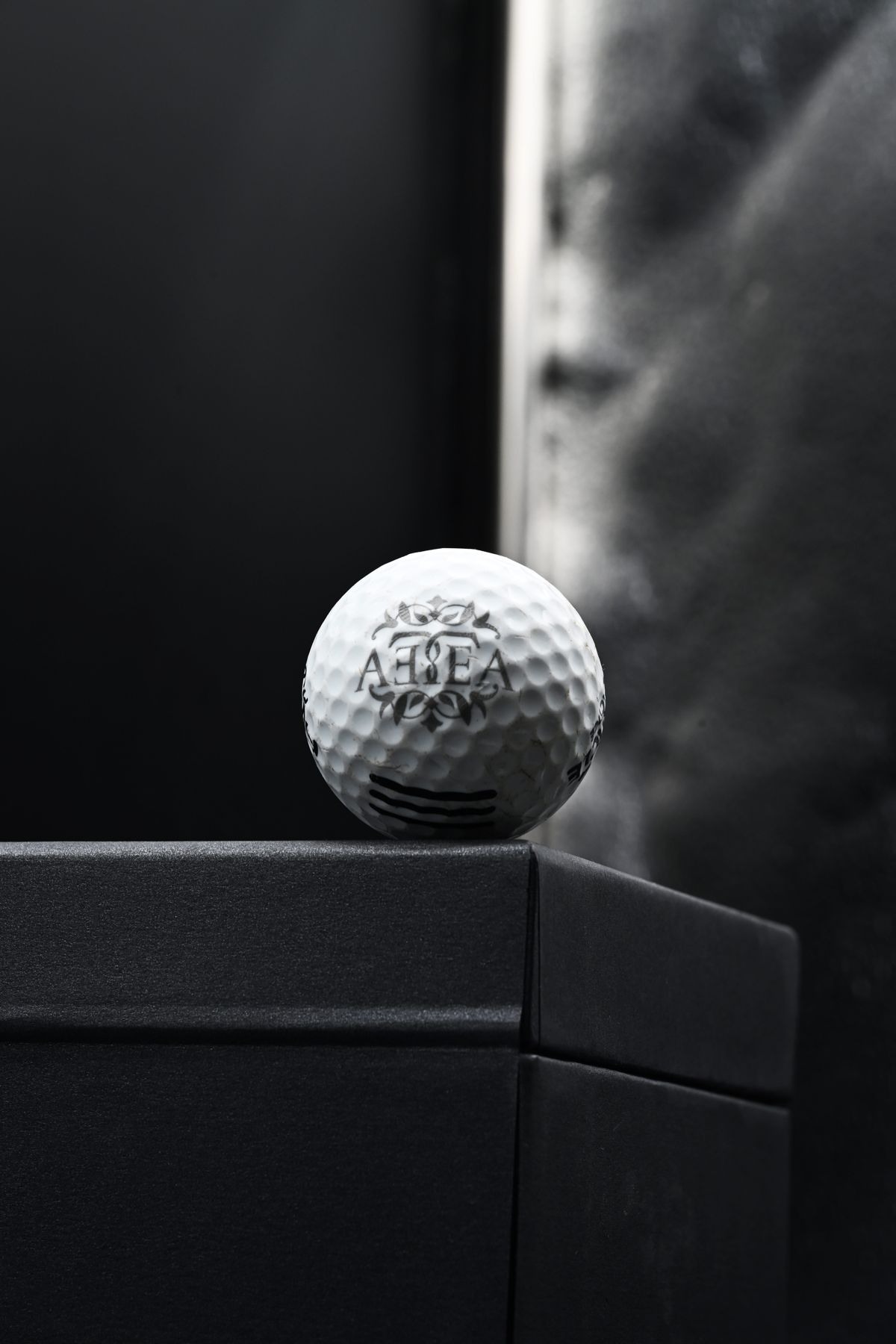Golf ball engraved with the AETEA logo on a black box